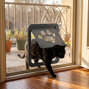 Chat noir passant par une chatière à volet sur porte-moustiquaire