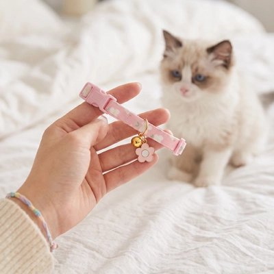 Collier chaton rose avec clochette dorée et pendentif fleur, présenté dans une main devant un chaton