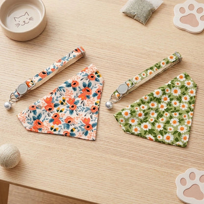 Deux bandanas pour chat avec collier à clip et grelot, modèles fleurs corail et marguerites verte et orange, posés sur une table en bois