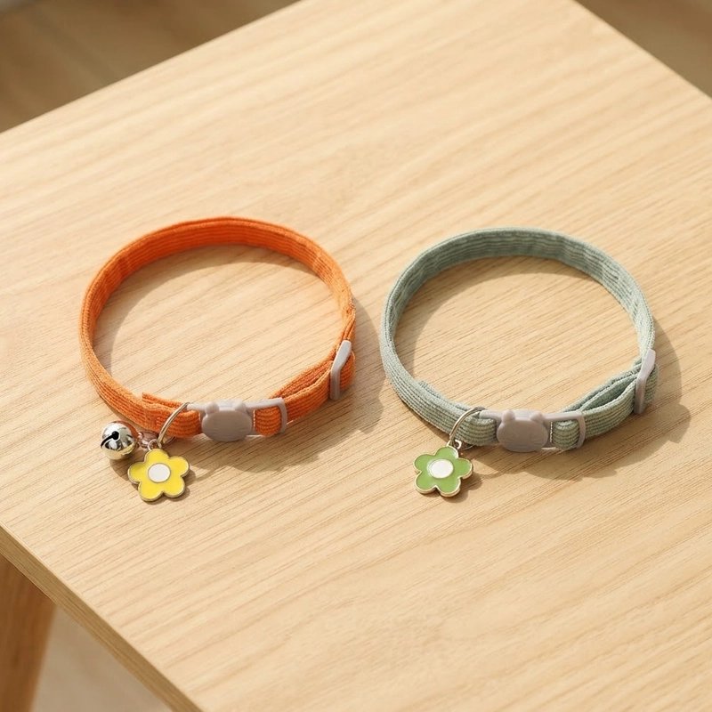 Deux colliers pour chat, un orange avec grelot et fleur jaune, un vert d'eau avec fleur verte, posés sur une table en bois