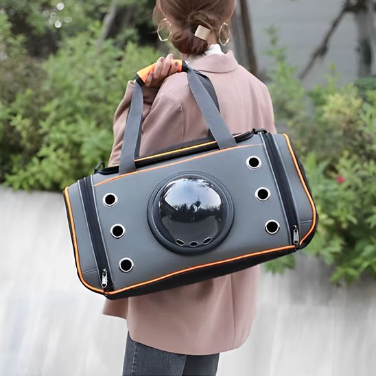 Femme de dos portant un sac de transport pour chat capsule gris orange en bandoulière en extérieur