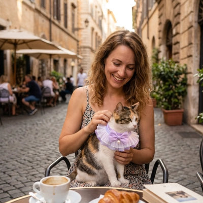 Femme souriante caressant son chat tigré portant un collier volanté lilas à perle, en terrasse dans une rue de Rome