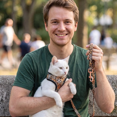Harnais chat léopard porté par un chat blanc, tenu dans les bras par un homme souriant en extérieur