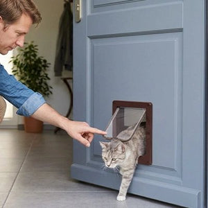 Homme guidant son chat tabby à travers une chatière pour chat marron installée sur une porte grise