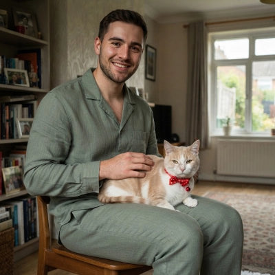 Homme souriant assis avec un chat blanc et roux portant un collier rouge à nœud papillon et grelot
