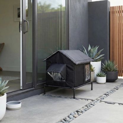 Niche pour chat extérieur noire posée sur pieds surélevés près d'une porte vitrée et de plantes