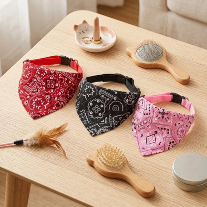 Trois bandanas pour chat rouge, noir et rose à motifs cachemire avec collier à clip, posés sur une table en bois