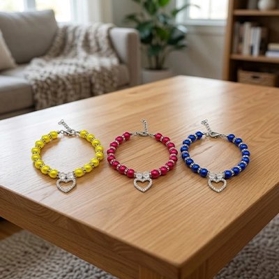 Trois colliers perles pour chat jaune rouge et bleu avec pendentif cœur strass posés sur une table